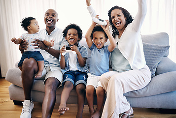 Image showing Happy young african american family sitting on a sofa in the living room at home and celebrating a win. Adorable mixed race boys playing video games with consoles while their parents cheer for them