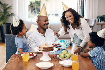 Image showing Happy african american family celebrating a birthday at home. Cheerful parents and their two kids laughing while wearing party hats. Boy receiving present from family on his birthday