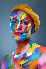 Image showing Color and I are one. Studio shot of a young woman posing with multi-coloured paint on her face and a french hat on her head.