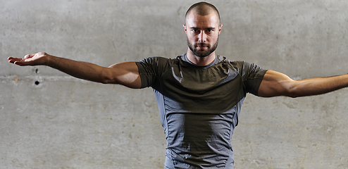 Image showing A muscular man working stretching exercises for his arms and body muscles in modern gym