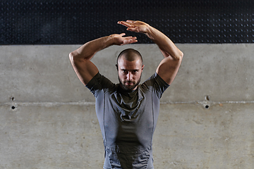 Image showing A muscular man working stretching exercises for his arms and body muscles in modern gym