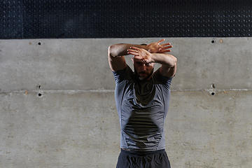 Image showing A muscular man working stretching exercises for his arms and body muscles in modern gym