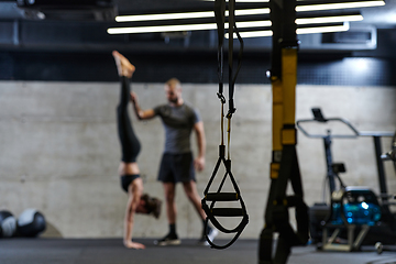 Image showing A muscular man assisting a fit woman in a modern gym as they engage in various body exercises and muscle stretches, showcasing their dedication to fitness and benefiting from teamwork and support