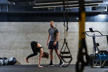 Image showing A muscular man assisting a fit woman in a modern gym as they engage in various body exercises and muscle stretches, showcasing their dedication to fitness and benefiting from teamwork and support