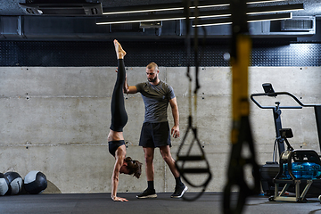 Image showing A muscular man assisting a fit woman in a modern gym as they engage in various body exercises and muscle stretches, showcasing their dedication to fitness and benefiting from teamwork and support