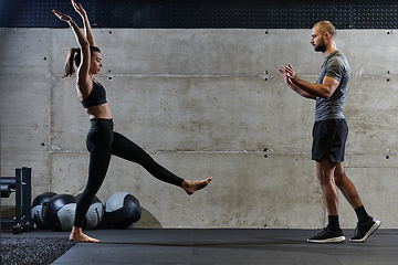 Image showing A muscular man assisting a fit woman in a modern gym as they engage in various body exercises and muscle stretches, showcasing their dedication to fitness and benefiting from teamwork and support