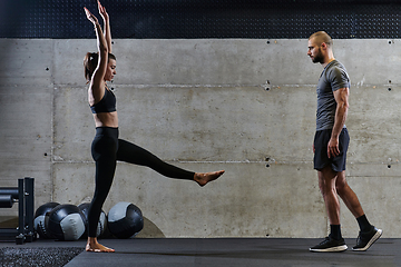 Image showing A muscular man assisting a fit woman in a modern gym as they engage in various body exercises and muscle stretches, showcasing their dedication to fitness and benefiting from teamwork and support