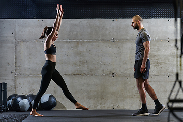 Image showing A muscular man assisting a fit woman in a modern gym as they engage in various body exercises and muscle stretches, showcasing their dedication to fitness and benefiting from teamwork and support