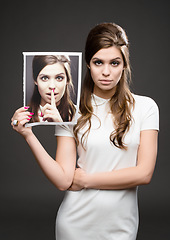 Image showing There are two sides to every story. Studio shot of an attractive young woman dressed up in 60’s wear and holding a photograph of herself whispering against a dark background.