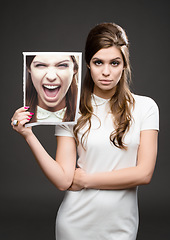 Image showing How I really feel inside. Studio shot of an attractive young woman dressed up in 60’s wear and holding a photograph of herself screaming against a dark background.