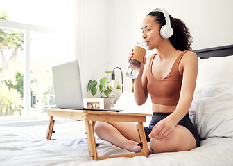 Image showing Dont forget to stay hydrated. a young woman using a laptop while sitting on her bed at home.