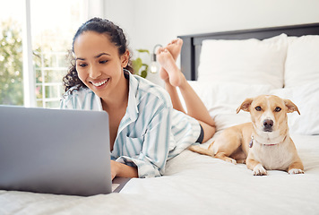 Image showing Home is where my dog is. a young woman using a laptop while relaxing on her bed at home.