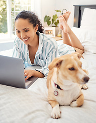 Image showing Chilling with my dog. a young woman using a laptop while relaxing on her bed at home.