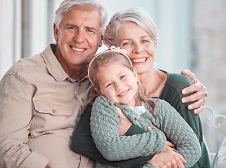 Image showing Little girl and her grandparents looking at the camera while sitting together at home. Cute girl bonding with her grandmother and grandfather. Loving couple spending time with their granddaughter