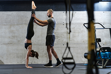 Image showing A muscular man assisting a fit woman in a modern gym as they engage in various body exercises and muscle stretches, showcasing their dedication to fitness and benefiting from teamwork and support