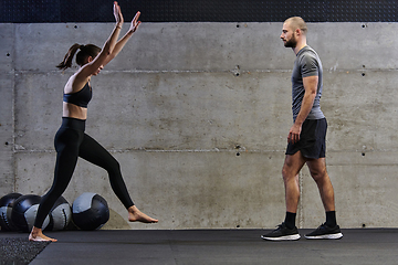 Image showing A muscular man assisting a fit woman in a modern gym as they engage in various body exercises and muscle stretches, showcasing their dedication to fitness and benefiting from teamwork and support