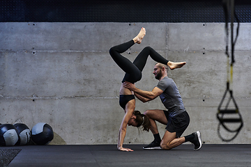 Image showing A muscular man assisting a fit woman in a modern gym as they engage in various body exercises and muscle stretches, showcasing their dedication to fitness and benefiting from teamwork and support