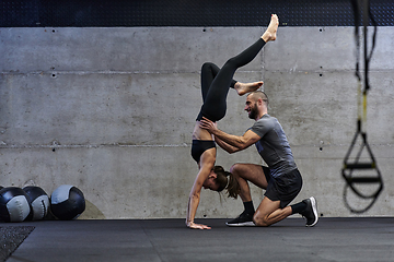 Image showing A muscular man assisting a fit woman in a modern gym as they engage in various body exercises and muscle stretches, showcasing their dedication to fitness and benefiting from teamwork and support