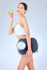 Image showing I like my products like my people non-toxic. Studio shot of a young woman tossing an apple while holding a scale against a grey background.