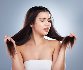 Image showing Young mixed race woman holding her long brown hair and looking at damaged split ends. Woman looking upset about hair care problems