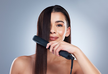 Image showing Beautiful young woman smiling while using a hair straightener on her long brown hair. Brunette woman using flat iron. Using hair care products to prevent heat damage