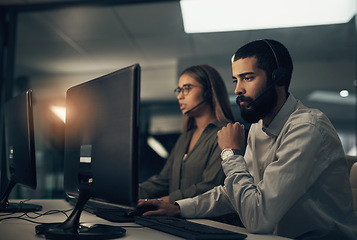 Image showing Let me look into it for you. a call centre agent working in an office alongside a colleague at night.