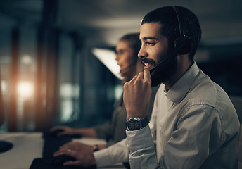 Image showing Its my pleasure to find the solutions for you. a call centre agent working in an office alongside a colleague at night.