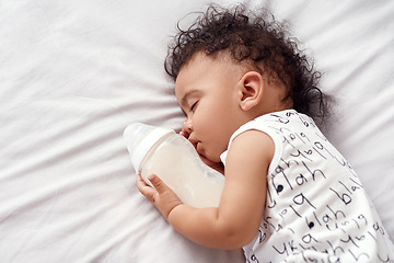 Image showing First comes the nom nom then comes the nap. an adorable baby boy sleeping with his bottle of milk on the bed at home.