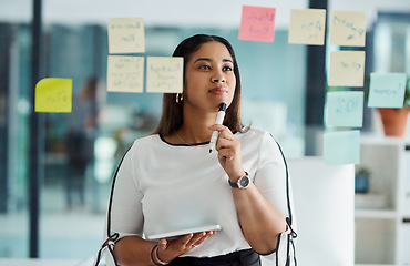 Image showing Thinking carefully about all her big ideas. a young businesswoman using a digital tablet while brainstorming with notes on a glass wall in an office.