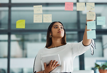 Image showing She has a plan to make big profits. a young businesswoman using a digital tablet while brainstorming with notes on a glass wall in an office.