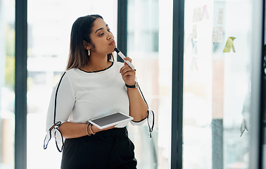 Image showing Delving into campaign creation. a young businesswoman using a digital tablet while brainstorming with notes on a glass wall in an office.