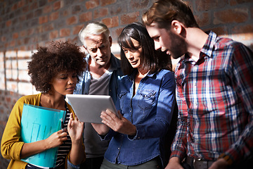 Image showing Finding some inspiration online. A group of colleagues standing around a digital tablet to assess designs.