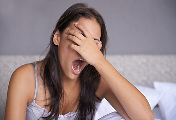 Image showing Can I go back to bed yet. a young woman sitting on a bed yawning.