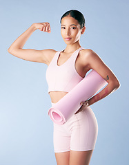 Image showing Mixed race fitness woman standing with her yoga mat and flexing her bicep in studio against a blue background. Beautiful young hispanic female athlete exercising or working out. Health and fitness