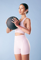 Image showing Mixed race fitness woman standing with a medicine ball or slam ball in studio against a blue background. Beautiful young hispanic female athlete exercising or working out. Health and fitness