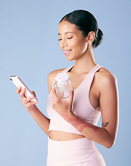 Image showing Mixed race fitness woman texting while break from her workout in studio against a blue background. Young hispanic female athlete sending a text message while taking a rest. Health and fitness