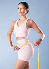 Image showing Mixed race fitness woman posing with a measuring tape around her waist in studio against a blue background. Young hispanic female athlete promoting exercise and a good diet to lose weight and get fit