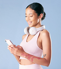 Image showing Mixed race fitness woman texting while break from her workout in studio against a blue background. Young hispanic female athlete sending a text message while taking a rest. Health and fitness