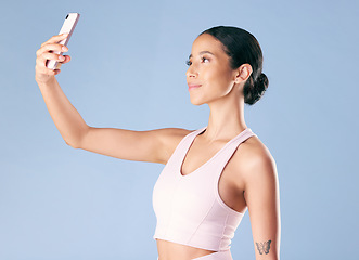 Image showing Mixed race fitness woman posing with her phone in studio against a blue background. Young hispanic female athlete taking selfie pictures with her smartphone to track her personal fitness growth