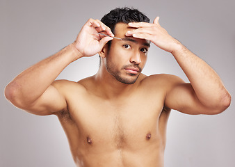 Image showing Handsome young mixed race man posing shirtless in studio isolated against a grey background. Hispanic male plucking his eyebrows with a tweezers. All part of his daily grooming and skincare routine