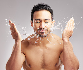 Image showing Handsome young mixed race man shirtless in studio isolated against a grey background. Hispanic male washing his face with water. Rinsing off his skin to keep it clean and hygienic as part of skincare