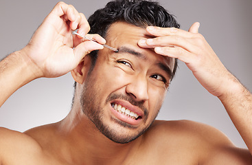 Image showing Handsome young mixed race man shirtless in studio isolated against a grey background. Hispanic male wincing in pain while plucking his eyebrows with a tweezers. Part of his daily grooming routine