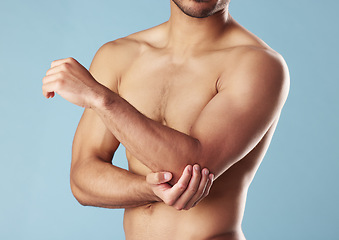 Image showing Closeup young mixed race man standing shirtless in studio isolated against a blue background. Unrecognizable topless male athlete suffering from an arm or elbow injury. Muscle cramp, ache or pain