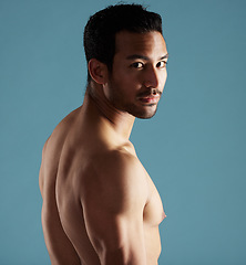 Image showing Handsome young hispanic man standing shirtless in studio isolated against a blue background. Mixed race topless male athlete looking confident, healthy and fit. Exercising to increase his strength