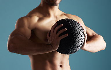 Image showing Closeup young hispanic man training with a medicine ball in studio isolated against a blue background. Mixed race shirtless male athlete exercising or working out to increase his strength and fitness