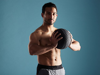 Image showing Handsome young hispanic man training with a medicine ball in studio isolated against a blue background. Mixed race shirtless male athlete exercising or working out to increase his strength and fitnes