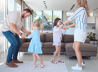 Image showing Caucasian family of four having fun and dancing together in the living room at home. Happy little playful girls bonding with mom and dad. Carefree loving parents entertaining their energetic daughter