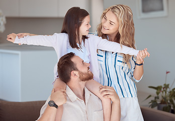 Image showing Happy caucasian family relaxing together at home. Carefree loving parents bonding with cute little daughter. Mom holding her adorable young playful girl while pretending to fly on her dads shoulders