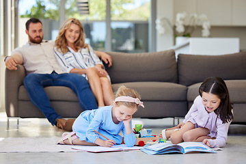 Image showing Two little sisters doing their homework together. Kids learning to read and write lying on living room floor with their parents watching in background