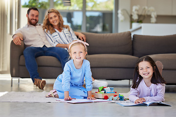 Image showing Two little girls doing homework lying on living room floor with their parents relaxing on couch. Little kids using colouring pencils and reading during family time at home